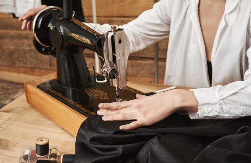 Seamstress working on new project. Female sewer working with fabric, creating fashionable garment with sewing machine in her workplace, being concentrated on needle to make seam look neat costurera